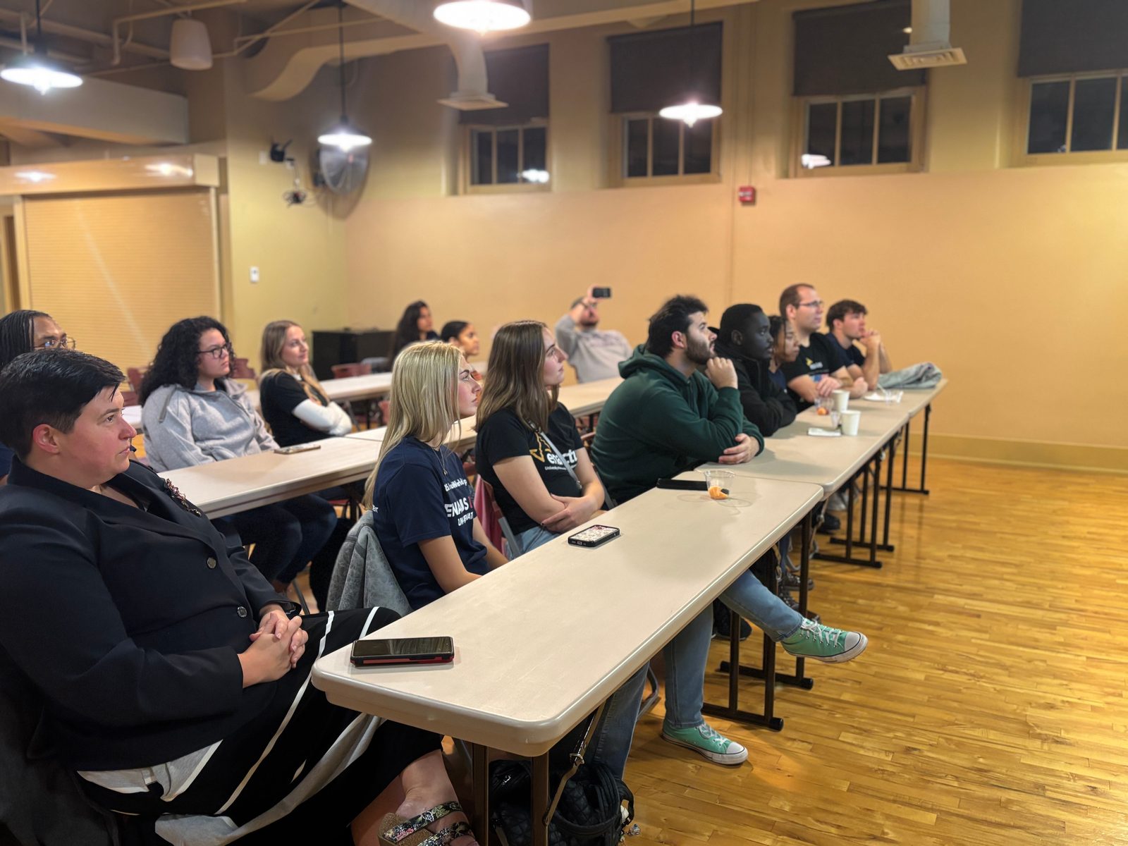 Enactus members and an advisor seated at long tables, listening to a speaker