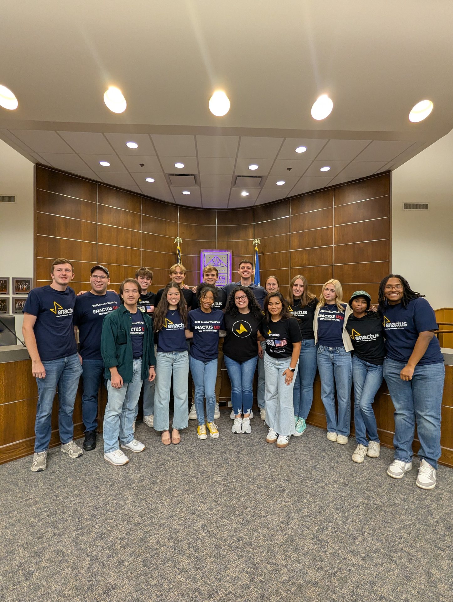 The team in Enactus shirts standing together in a city council chamber