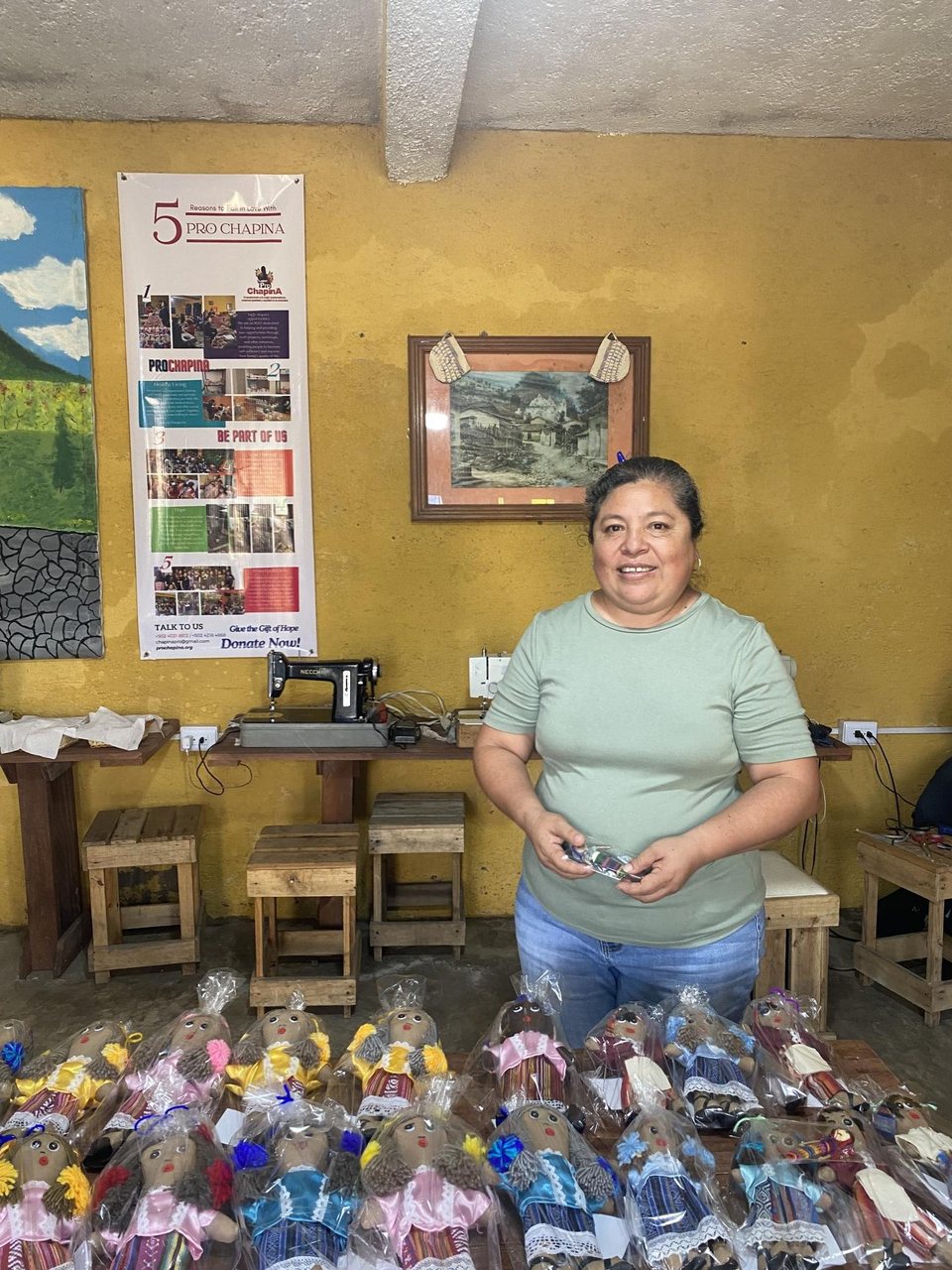 A ProChapina member smiling behind a table of handmade dolls in the workshop